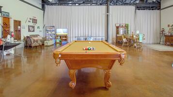 A billiards table in a room with a pool table, a television, and various items on shelves.