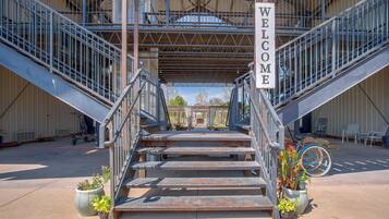 A metal staircase leading to a covered area with a 'WELCOME' sign, surrounded by potted plants and outdoor seating.