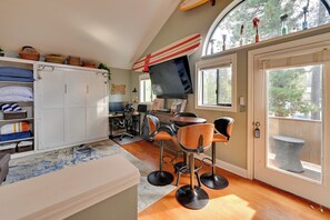 A compact living space with a kitchenette, a dining area with bar stools, a television mounted above the counter, and a large window providing a view of the outdoors. - 1 Mi to Sunriver Resort! Studio w/ Hot Tub Access (Sunriver)