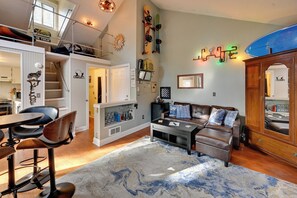 A spacious living room with a high ceiling, a built-in kitchen, a dining area, and a cozy seating area with a fireplace. - 1 Mi to Sunriver Resort! Studio w/ Hot Tub Access (Sunriver)