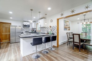 A modern kitchen with a central island, bar stools, a dining area with a table and chairs, and a large window with a view. - 4 Mi to Big Boulder! Pocono Family Retreat (Blakeslee)