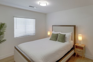 Un dormitorio con cama, lámparas de noche, ventana con persianas y un respiradero en el techo.