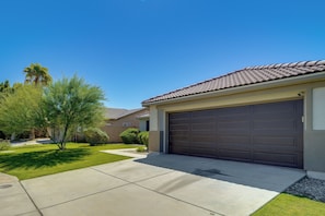 A residential driveway leading to a garage with a tiled roof, surrounded by a well-maintained lawn and a variety of trees. - Coachella Getaway w/ Yard! Near Festivals & Golf (Coachella)