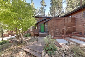 Une cabane en bois avec une porte verte, une terrasse en bois et un chemin de pierres menant à l’entrée.