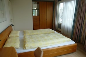 Un dormitorio con una cama, un armario de madera, un espejo y una ventana con cortinas.