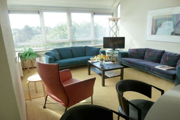 Una sala de estar con un sofá azul, una silla roja, una silla negra, una mesa de centro y un televisor.