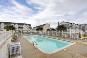 Une piscine entourée d’une clôture blanche, avec des chaises longues et un ciel dégagé.