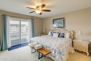 Ein Schlafzimmer mit einem Bett, einem Nachttisch, einer Lampe, einem Deckenventilator und Blick auf Gebäude.