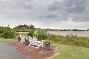 Une vue sur le lac, avec des fauteuils Adirondack et des plantes en pot, une pelouse et une rangée de maisons en arrière-plan.