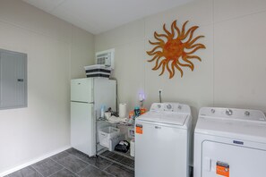 A laundry room with two Maytag washers, a dryer, a metal rack with laundry baskets, and a wall-mounted heater.