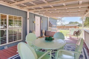 Eine überdachte Terrasse mit Tisch, Stühlen, einer Tür und Blick auf den Garten.