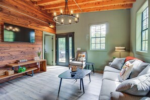Ein geräumiges Wohnzimmer mit Holzboden, einem flachbildfernseher an der Wand, einem Sofa, einem Couchtisch und einem Sessel.