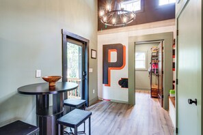 Un pasillo con suelo de madera, una mesa redonda con dos sillas, una decoración con la letra 'P' en la pared y una puerta que da a otra habitación.