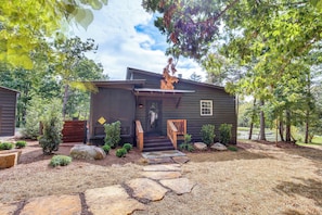A rustic cabin with a stone pathway leading to the entrance, surrounded by trees and a small pond. - Peaceful Cabin on Pond w/ Hot Tub & More! (Lookout Mountain)