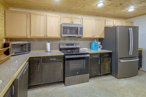 A kitchen with wooden cabinets, a microwave, a toaster, a coffee maker, a refrigerator, and a dishwasher. - Lakefront Greers Ferry Rustic Getaway w/ Game Room (Greers Ferry)