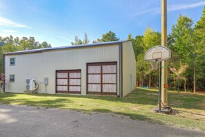 A single-story building with a metal exterior, two large garage doors, and a basketball hoop. - Lakefront Greers Ferry Rustic Getaway w/ Game Room (Greers Ferry)