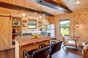 A wooden interior with a kitchen area featuring a wooden table, chairs, a microwave, and a refrigerator. - Refined Rustic Retreat: Custom Designed by Owners (Washington)