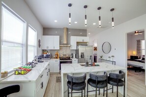 A modern kitchen with a central island, bar stools, and a dining area with a bench. - Community Boat Ramp! Family Escape w/ Fenced Yard (Granbury)