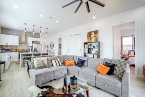 A modern living space with a grey sectional sofa, a glass coffee table, and a kitchen area with white cabinets and a dining set. - Community Boat Ramp! Family Escape w/ Fenced Yard (Granbury)