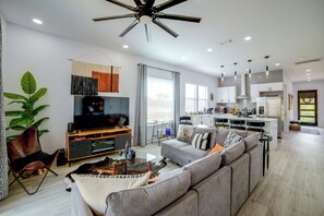 A modern living room with a large flat-screen TV, a grey sofa, and a ceiling fan. - Community Boat Ramp! Family Escape w/ Fenced Yard (Granbury)