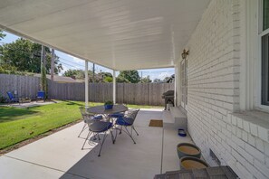 A covered patio with a table and chairs, a wooden fence, and a grassy yard. - Charming Tulsa Home near LaFortune Park (Tulsa)