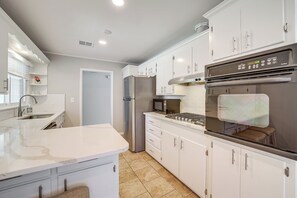 A modern kitchen with white cabinetry, stainless steel appliances, and a large island. - Charming Tulsa Home near LaFortune Park (Tulsa)