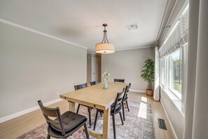 A dining room with a wooden table, chairs, a hanging light fixture, a potted plant, and a window with blinds. - Charming Tulsa Home near LaFortune Park (Tulsa)