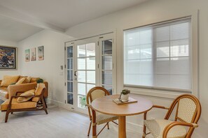 A room with a dining area featuring a round wooden table and wicker chairs, a sofa with cushions, and a door leading outside. - Walk to Beach & Dtwn! Extended San Clemente Escape (San Clemente)