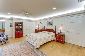 Ein Schlafzimmer mit Bett, Kommode, Nachttisch und einem großen Fenster.