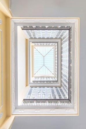 Blick durch ein Fenster mit geometrischem Muster, das zu einem Oberlicht und einer gemusterten Decke führt.