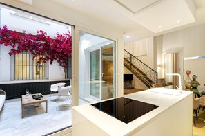 Ein modernes Interieur mit einer Glastrennwand, einem Essbereich mit Tisch und Stühlen, einer Treppe und einem Balkon mit pinkfarbenen Blumen.
