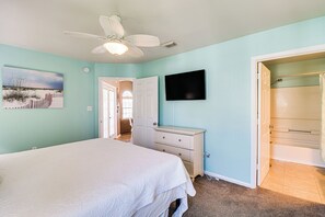 Ein Schlafzimmer mit Bett, Schminktisch, Deckenventilator, Fernseher und einer Tür zu einem Badezimmer.