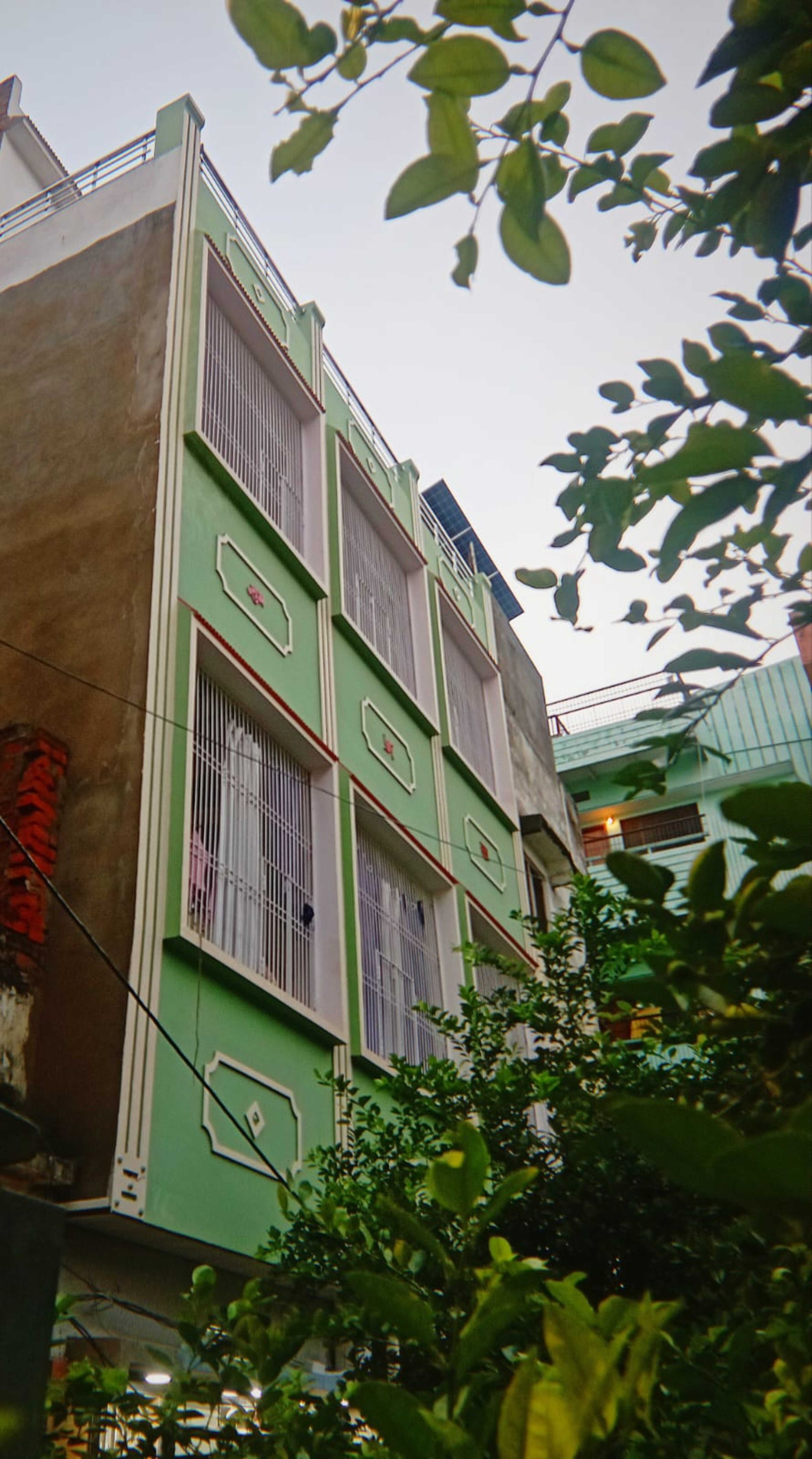 Un edificio de varios pisos con ventanas protegidas por barrotes y fachada verde.
