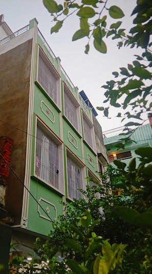Un edificio de varios pisos con ventanas protegidas por barrotes y fachada verde.