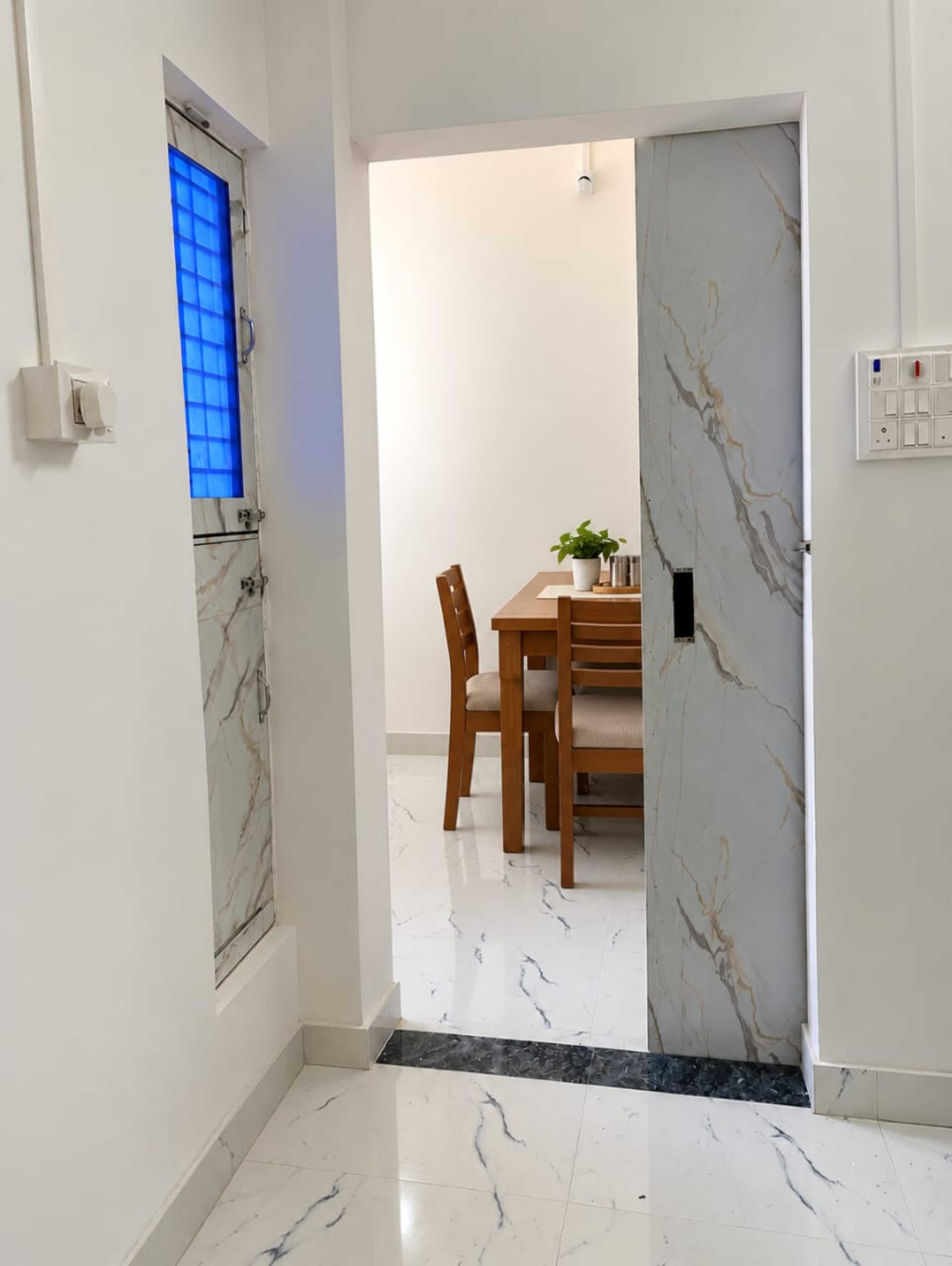 Un pasillo con piso de mármol que conduce a un comedor con mesa y sillas.