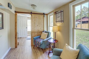 Een kamer met een houten vloer, een blauwe bank met een gestreept plaid, een kleine tafel met een lamp en een wandklok.