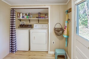 Een wasruimte met een wasmachine, droger en planken met schoonmaakmiddelen.