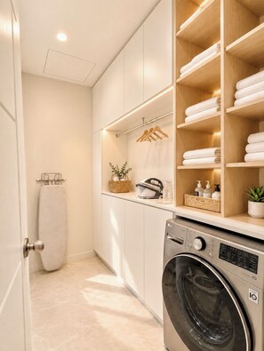 Een moderne wasruimte met een wasmachine, keurig geordende planken met handdoeken en een mand met toiletartikelen.