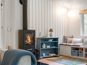 Ein gemütliches Zimmer mit Kaminofen, einem blauen Regal, einem Fenster mit Jalousien und einem Bett mit gestreifter Bettwäsche.
