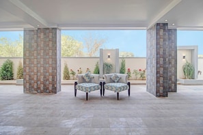 Amplia zona de patio con dos sillones y una mesa, rodeada de pilares de piedra y vistas a un jardín.
