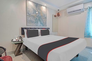 Una habitación de hotel con una cama grande, una mesita de noche con hervidor, un espejo y un equipo de aire acondicionado.