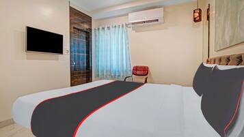 Quarto de hotel com cama, televisão, ar condicionado, uma cadeira vermelha e janela com cortinas.