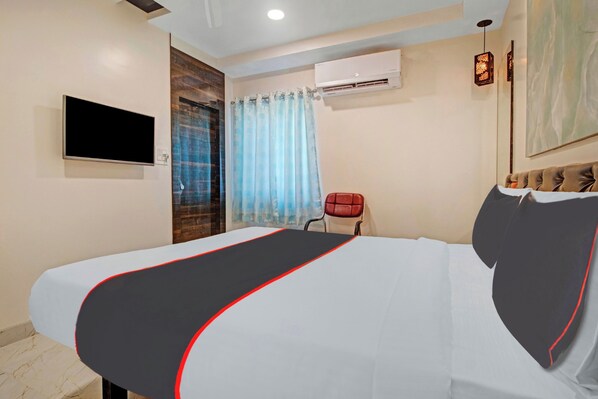 A hotel room with a bed, a television, an air conditioning unit, a red chair, and a window with curtains. - Collection O Halcyon SS Grand (Hyderabad)