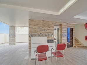 A reception area with a modern design, featuring a reception desk, two red chairs, and a wall-mounted security camera. - Collection O Halcyon SS Grand (Hyderabad)
