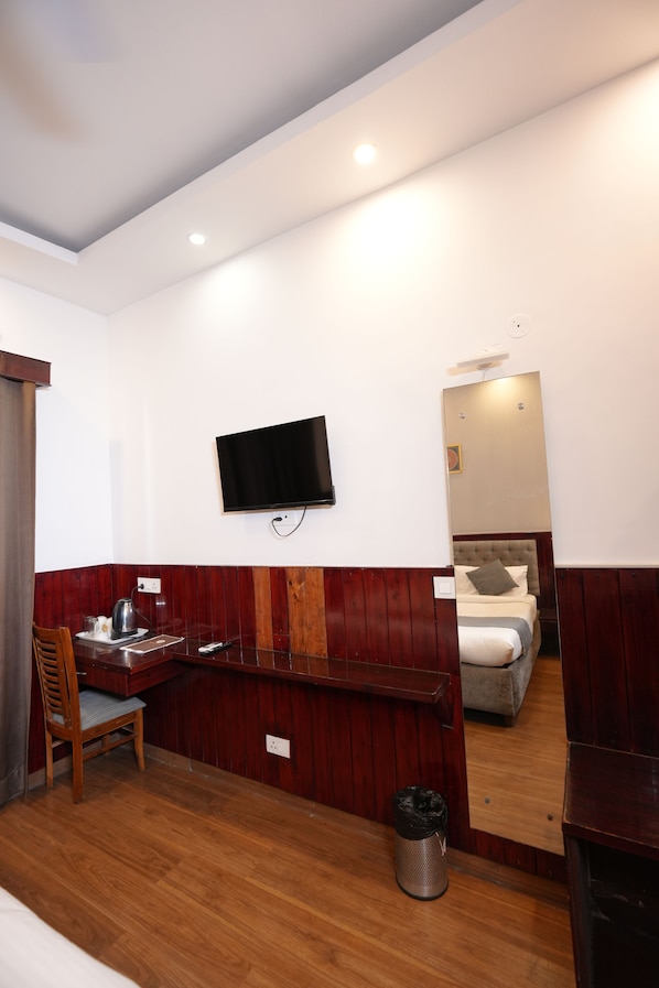 Habitación de hotel con un escritorio de madera, una silla, un televisor montado en la pared, una cama con cabecera y un espejo que refleja la habitación.
