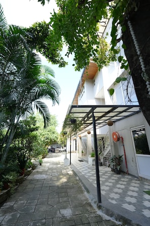 Un camino bordeado de plantas en macetas que conduce a un edificio con un espacio exterior cubierto.