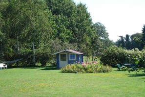 A small blue structure with a red roof, surrounded by a grassy area with flowers and trees. - House Seamark / Studio (Born)