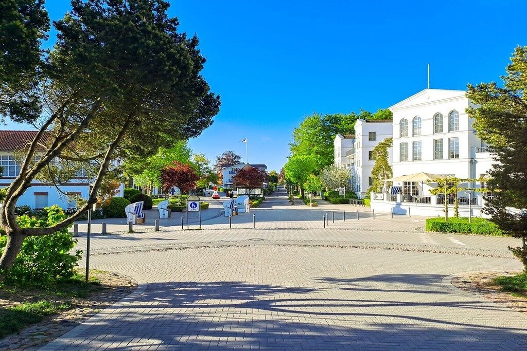 A paved square with a white building in the background, surrounded by trees and greenery.