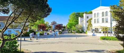 A paved square with a white building in the background, surrounded by trees and greenery.