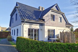 A two-story house with a sloped roof, a visible chimney, and a fenced backyard. - Holiday home in Zingst with swimming pool (Zingst)